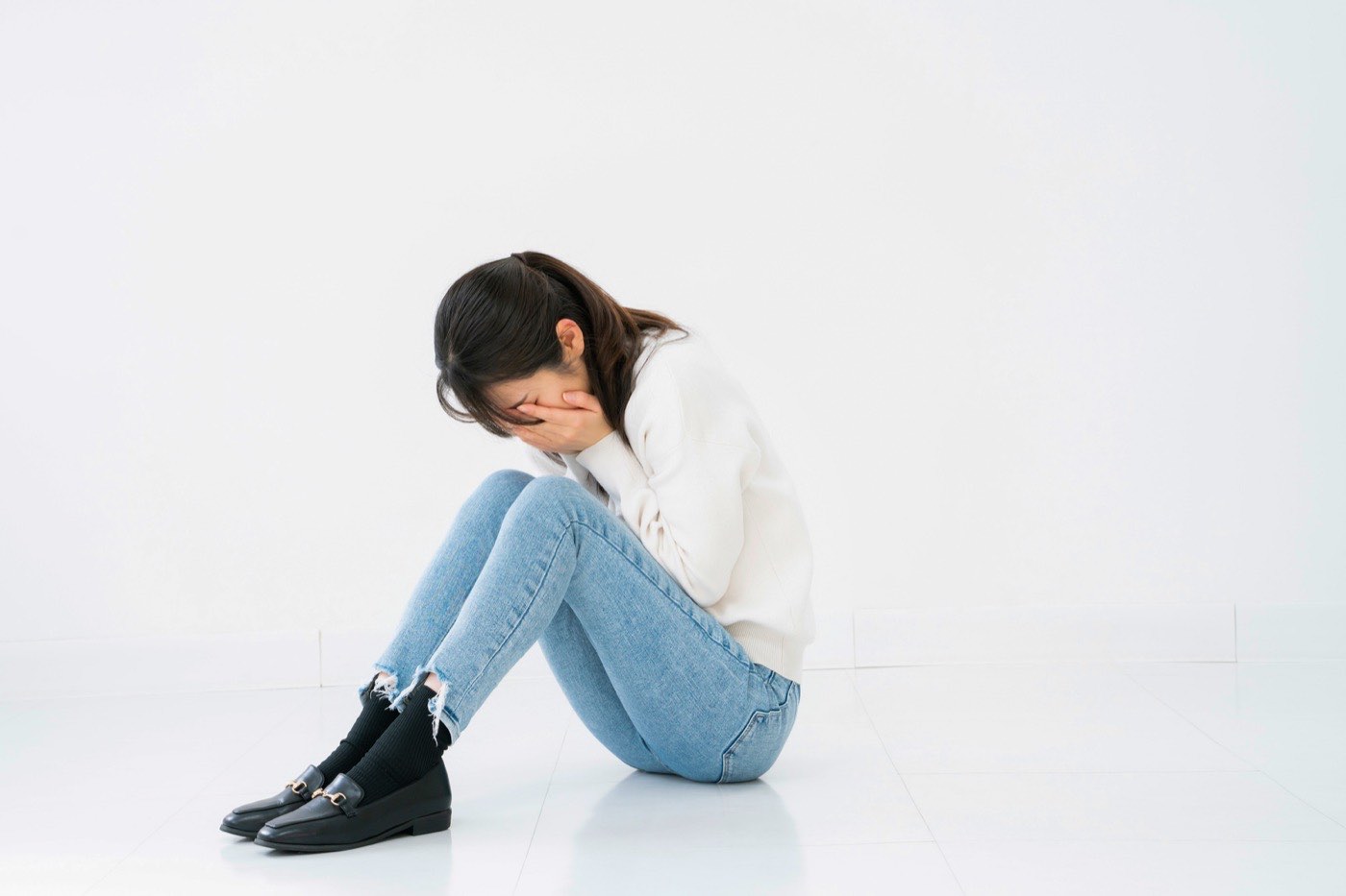 膝を抱え、顔を覆ってうずくまる女性