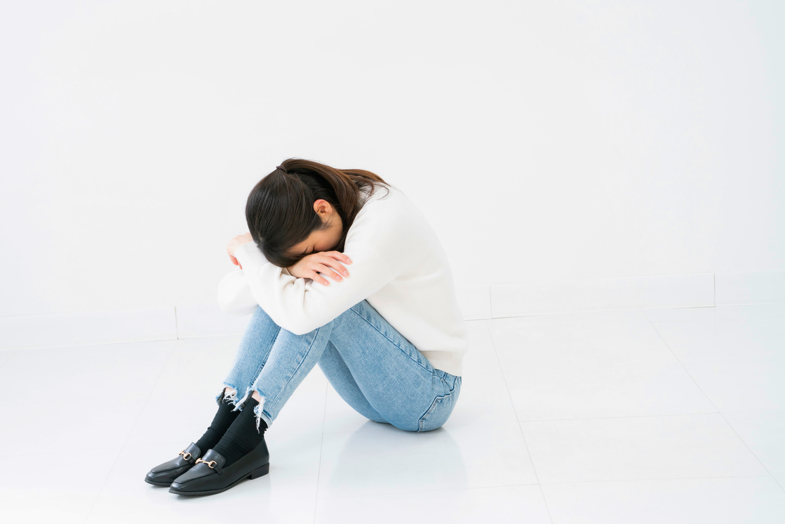 床に座り込み、膝に顔をうずめてうつむく女性