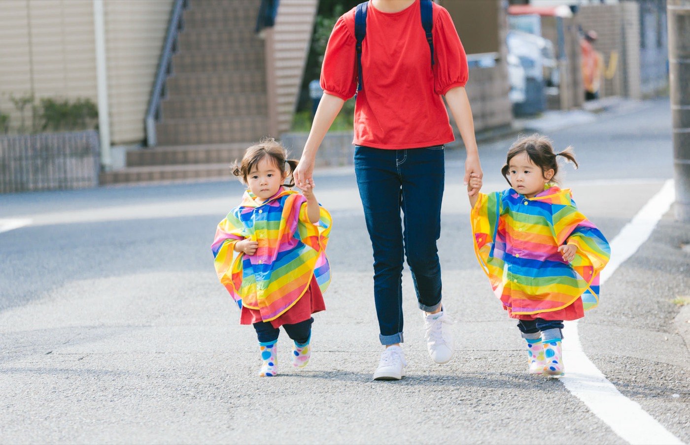 歩道を母親と手をつないで歩く双子の女の子