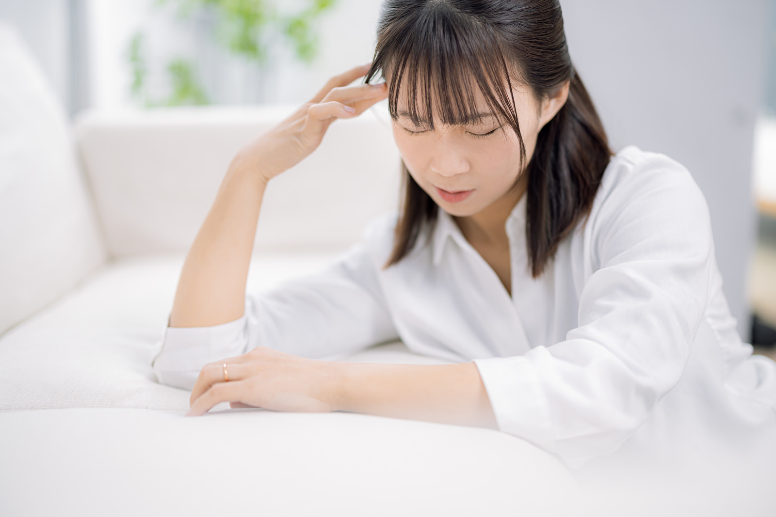 ソファで頭に手をやり、うつむいて悩んでいる女性