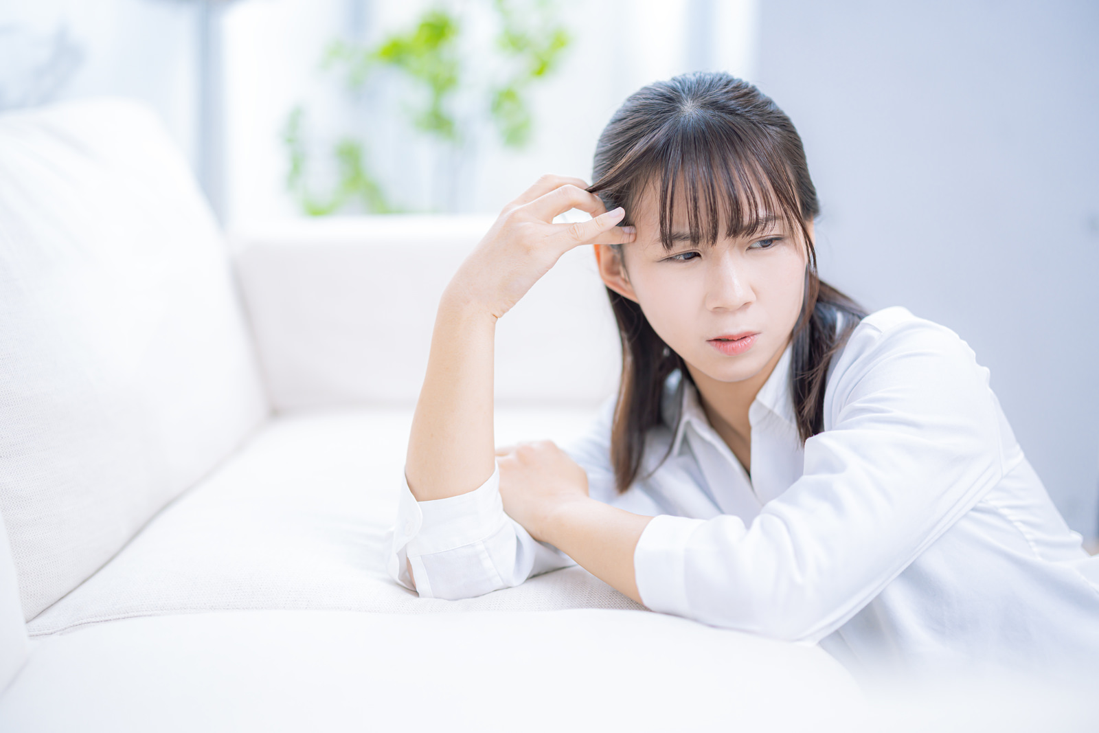 ソファにもたれ、頭に手をあてて考えこむ女性